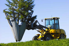 A skid steer loader equipped with a Baumalight tree spade attachment, featuring dual hinged blades, is positioned on grass with a clear blue sky in the background.